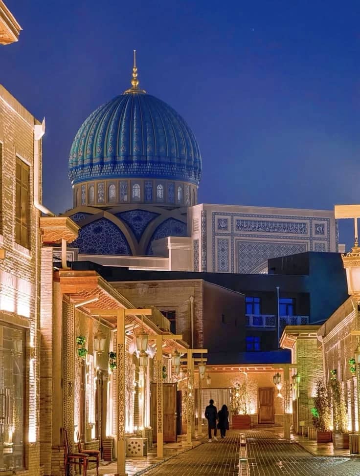 A lamplit old-town street at dusk under a blue tiled dome