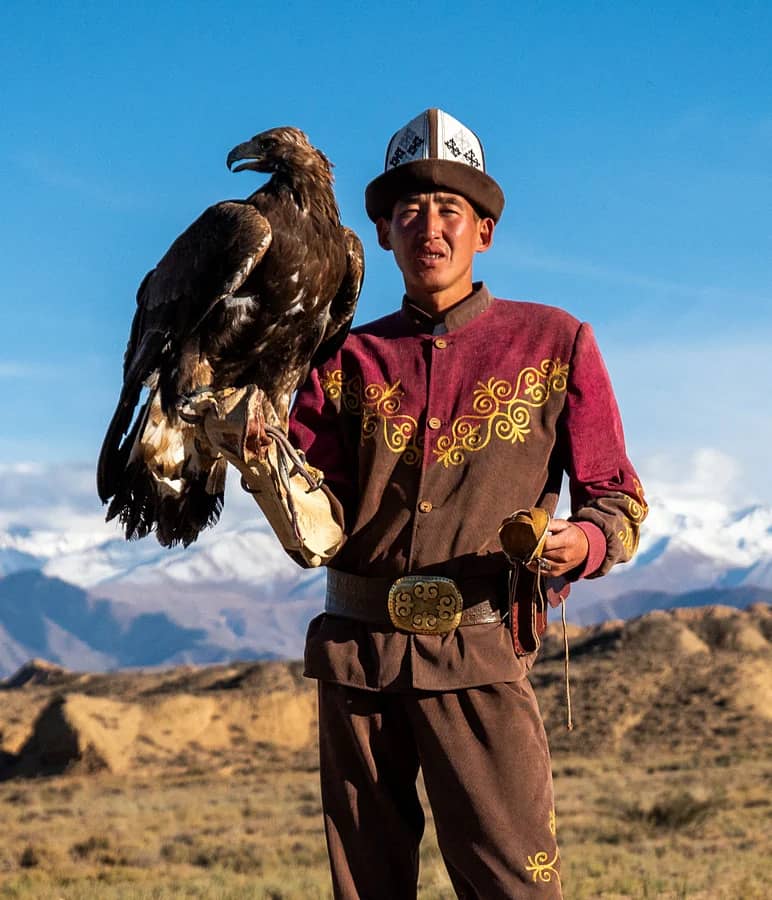 A Kyrgyz eagle hunter with his golden eagle, snow peaks behind