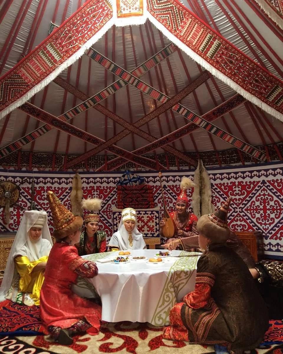 Women in festive dress round a table inside a decorated yurt